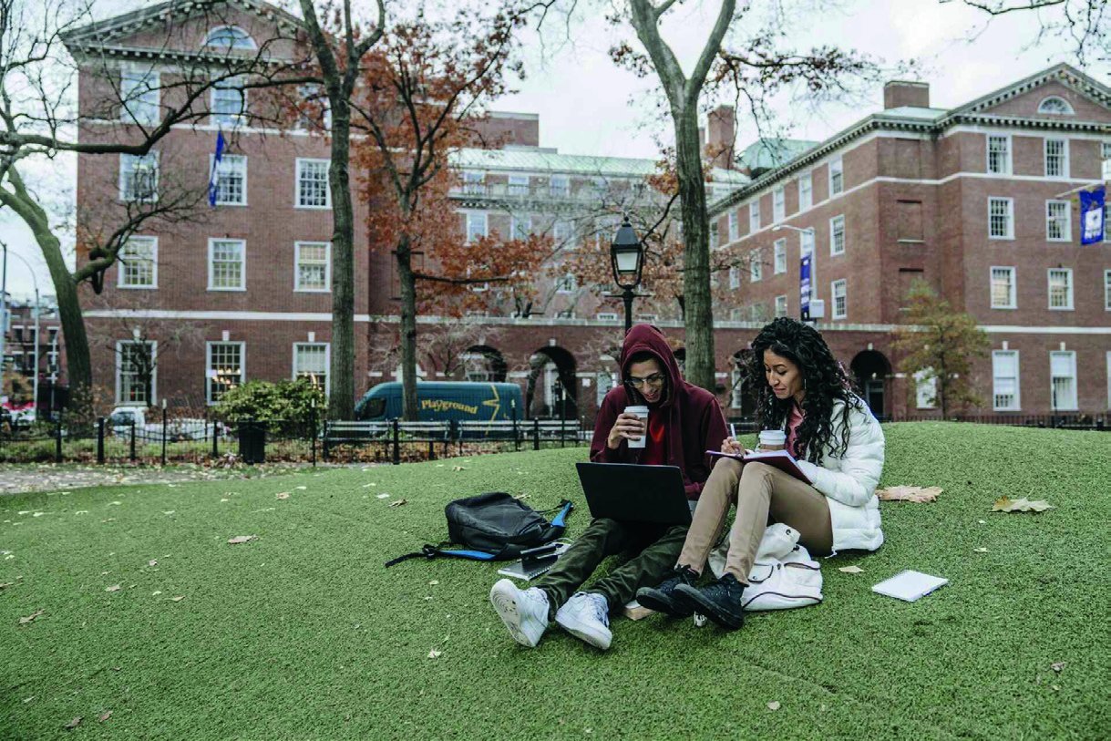 Students on a university campus lawn researching universities